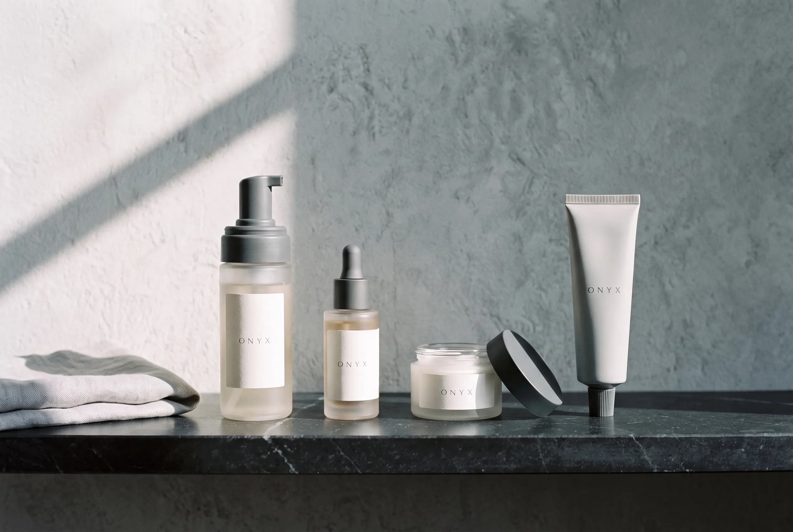 A four-step Onyx Skin Co. routine laid out in order on a stone shelf: cleanser, serum, moisturizer and sunscreen.